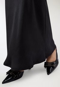 Scarpe nere con punta a punta lucida, caratterizzate da un fiocco strutturato adornato con occhielli metallici e un tacco basso.