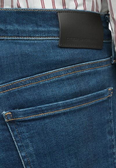 Sötét mosású farmernadrág, barna varrással, a derékrészen fekete bőr címkével, amelyen a "CITIZENS of HUMANITY" felirat domborított.