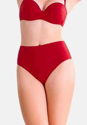 Donna che indossa un costume da bagno rosso a due pezzi con slip a vita alta e top stile balconcino su sfondo semplice.