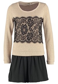 Pull beige en maille texturée, avec un voile de dentelle noire à l'avant. Jupe évasée noire en dessous, créant un effet superposé.