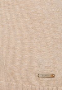 Pull tricoté pêche clair avec une texture lisse. Comprend une petite étiquette argentée marquée "Esprit" près de l'ourlet.