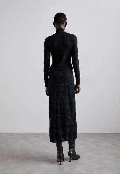 Top de manga larga negro con estampado, combinado con una falda negra a la altura del tobillo. El conjunto presenta un diseño ajustado y una tela texturizada.