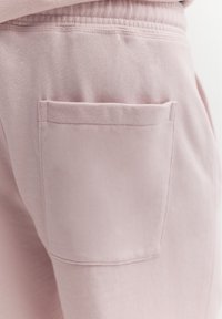 Détail de la poche arrière sur un pantalon décontracté en tissu doux rose clair avec taille élastique.