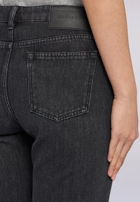 Les jeans en denim noir présentent une coupe ajustée, une texture subtile et une étiquette en cuir avec le logo "Trussardi" au niveau de la taille.