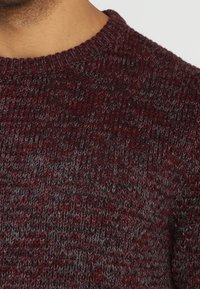 Pull tricoté dans des tons bordeaux foncé et gris. Présente un col rond et un motif texturé, avec une épaisseur moyenne et un tissu doux.