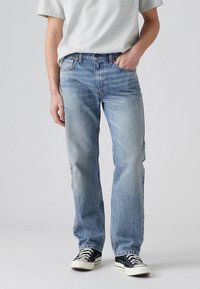 Person som bär ljusblå jeans med raka ben, en grå kortärmad tröja och svarta sneakers med låg överdel och vita skosnören.