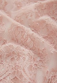 Tissu en dentelle rose clair délicate avec des motifs floraux et une texture fine en maille, délicatement drapé et légèrement plié.