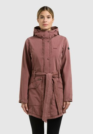 Donna che indossa una giacca con cappuccio color malva, con cintura, tasche frontali, bottoni a pressione e maniche lunghe, su sfondo grigio uniforme.