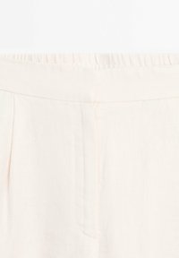 Des pantalons en lin rose clair présentent une taille élastique, des plis, et une texture lisse, avec un léger brillant et des poches latérales.