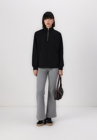 Svart zip-up hettegenser med lange ermer, kombinert med grå flagrende bukser. Svart joggesko med beige såle og en liten brun skulderveske.