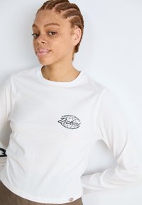 Bijela majica dugih rukava od pamuka, s crnim grafičkim prikazom globusa i riječju "Dickies" na lijevoj strani prsnog područja.