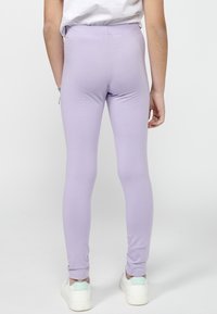 Leggings lilas en mélange de coton extensible, avec un design ajusté, une taille élastique et une texture lisse. Associés à des baskets blanches.