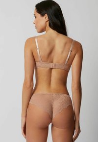 Lace bh en string set in nude, voorzien van ingewikkelde bloemmotieven, verstelbare schouderbandjes en een gekartelde rand op de string.
