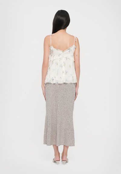 Bluză fără mâneci, crem, cu imprimeu floral și margine în straturi, complementată de o fustă midi bej cu stropi. Ambele articole au detalii rafinate.