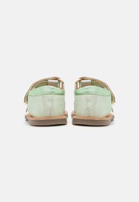 Sandalias metálicas verdes con una textura suave, diseño de espalda abierta, correa ajustable y suelas planas, que muestran un estilo simple y funcional.