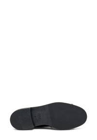Suela de zapato de cuero negro con superficie texturizada, forma redondeada y logotipo de marca en relieve; diseño minimalista con tacón plano y bordes suaves.