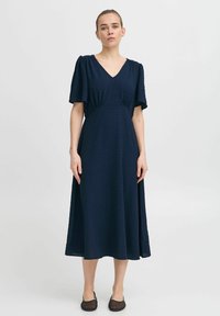 Navy blue midi dress with a V-neck, short flutter sleeves, textured dots, and a fitted waist, flowing into a loose, A-line silhouette.