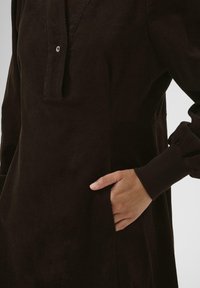 Braunes Cordkleid mit lockerer Passform, Knopfleiste vorne und langen, gerafften Ärmeln; enthält seitliche Taschen und eine strukturierte Oberfläche.