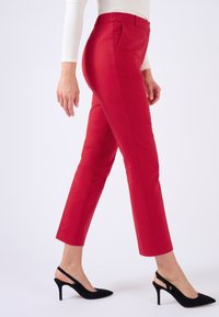 Pantalones rojos de corte ajustado y longitud recortada, hechos de una tela suave. Combinados con tacones slingback negros.