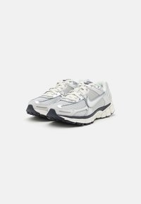 Scarpe da corsa Nike con una tomaia in rete argentata e bianca con accenti riflettenti, lacci rotondi e suola in gomma nera.