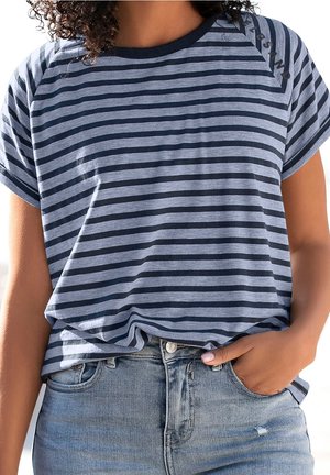 Femme portant un t-shirt à manches courtes rayé bleu marine et gris, légèrement rentré dans un jean en denim bleu clair, avec une main dans la poche.