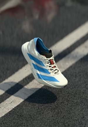 Hvid og blå sportssko i luften over asfalt med hvide linjer, som viser bevægelse og sportslige designelementer inklusive snørebånd og branding.