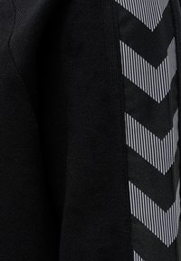 Maglione nero con un tessuto a maglia testurizzato da un lato e un tessuto a righe con motivo a zigzag dall'altro, che offre un contrasto visivo interessante.