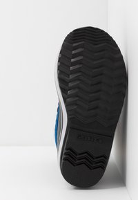 Czarna gumowa podeszwa sportowego buta z zygzakowatym wzorem, z niebieskimi bokami i białymi akcentami, z widoczną marką "SOREL".