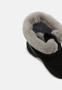 Schwarzer Stiefel mit einem weichen, grauen Pelzfutter am oberen Rand, ausgestattet mit einem strukturierten Obermaterial und einer robusten Gummisohle.