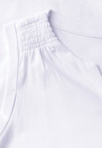Top de algodón blanco con escote fruncido y textura suave. Diseño simple sin patrones ni acentos.