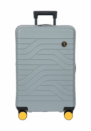 Grauer Hartschalenkoffer mit schwarzem Griff, gelben Rollen und Wellenmuster auf der Vorderseite.