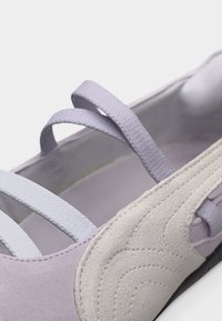 Κοντινή λήψη μοβ πλατφόρμας με δύο ελαστικές τιράντες στο πάνω μέρος και επικάλυψη από μπεζ σουέτ με ραμμένες λεπτομέρειες.