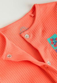 Body bébé côtelé corail avec boutons-pression et un petit patch carré présentant des baies rouges sur fond bleu.