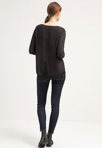 Sort langærmet top med lige kant og slids bagpå, parret med mørke skinny jeans og ankelstøvler. Glat stofstruktur.