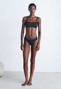 Čierny bavlnený crop top a zodpovedajúce nohavičky. Top má tenké ramienka. Nohavičky majú pás s logom a názvom značky v bielej farbe.