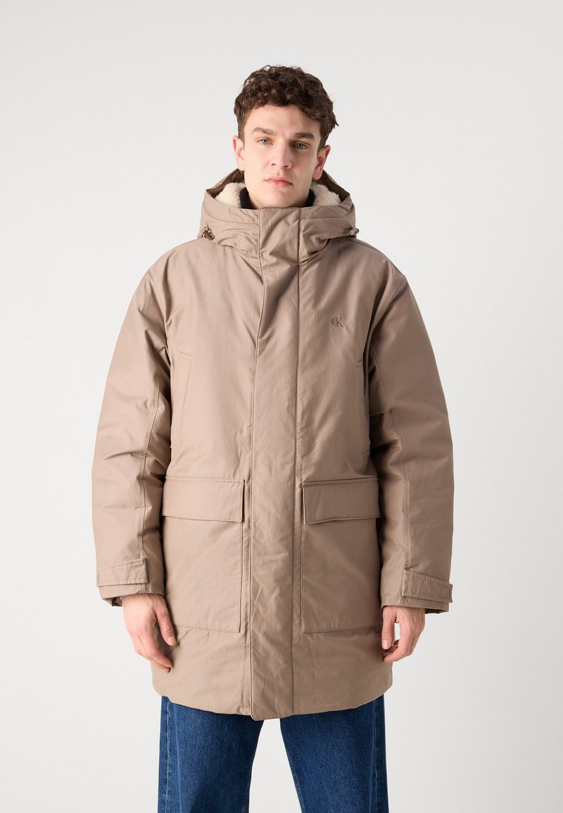 Beige gewatteerde parka-jack met een hoge kraag en verstelbare capuchon. Voorzien van twee voorzakken en een zachte textuur.