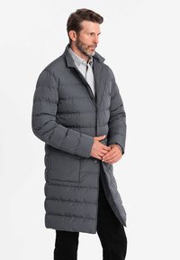 Piumino grigio con zip, colletto alto e motivo a righe orizzontali. Presenta una tasca frontale e un design di lunghezza media.