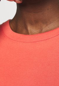 Coral cotton t-shirt with a ribbed crew neckline. Smooth texture and even stitching along the edge. Close-up of the neckline area.