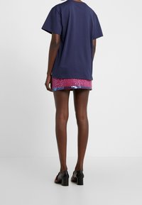 Camisa de algodón azul marino de mangas cortas, combinada con una falda rosa con lentejuelas y lunares, vista desde la parte posterior. Zapatos de tacón cuadrado negros.