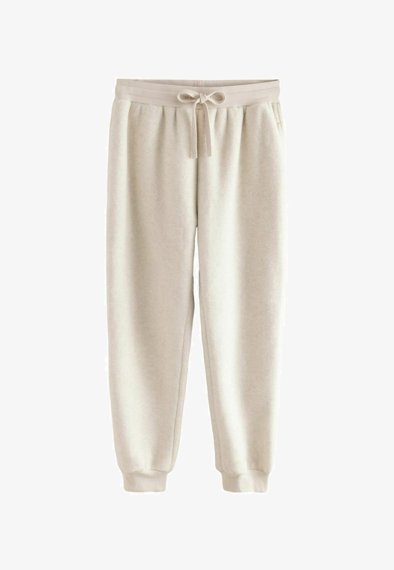 Unos pantalones de chándal color beige claro en una tela suave cuentan con una cinturilla elástica con cordón y puños ajustados en los tobillos.