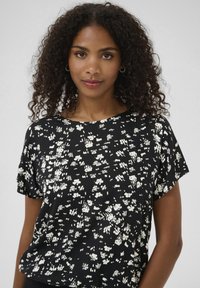 Black short-sleeve top featuring a white abstract floral pattern, made from lightweight fabric with a relaxed fit and round neckline.