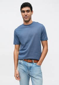 Modra bombažna majica s kratkimi rokavi, okrolim izrezom, kombinirana s svetlo modrimi kavbojkami in rjavim pasom. Gladek tekstura, oprijet kroj.