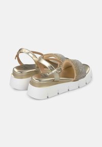 Goldene metallische Sandalen mit dekorativen Strasssteinen, verstellbarem Riemen und einer dicken weißen Plateausohle. Glatte Textur und offenes Design.