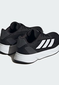 Scarpe da ginnastica nere con una tomaia in tessuto testurizzato, caratterizzate da tre strisce bianche e dettagli grigi sul tallone e sul midsole.