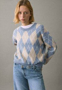 Maglione a rombi in azzurro chiaro e beige con scollatura rotonda, morbida trama e polsini a costine, abbinato a jeans dritti azzurri chiari.