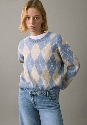 Suéter de punto en azul claro y beige con diseño argyle, escote redondo, textura suave y puños de canalé, combinado con jeans rectos de azul claro.