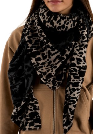 Femme portant une veste zippée marron avec une grande écharpe léopard noir et gris enroulée autour de son cou.