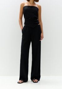 Haut noir sans bretelles associé à un pantalon noir ample. Le tissu est fluide, avec une texture lisse. Des sandales à fines lanières noires complètent la tenue.