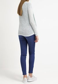 Lichtblauwe, gestructureerde trui met lange mouwen, gedragen over donkere skinny jeans en witte sneakers, bekeken van achteren.