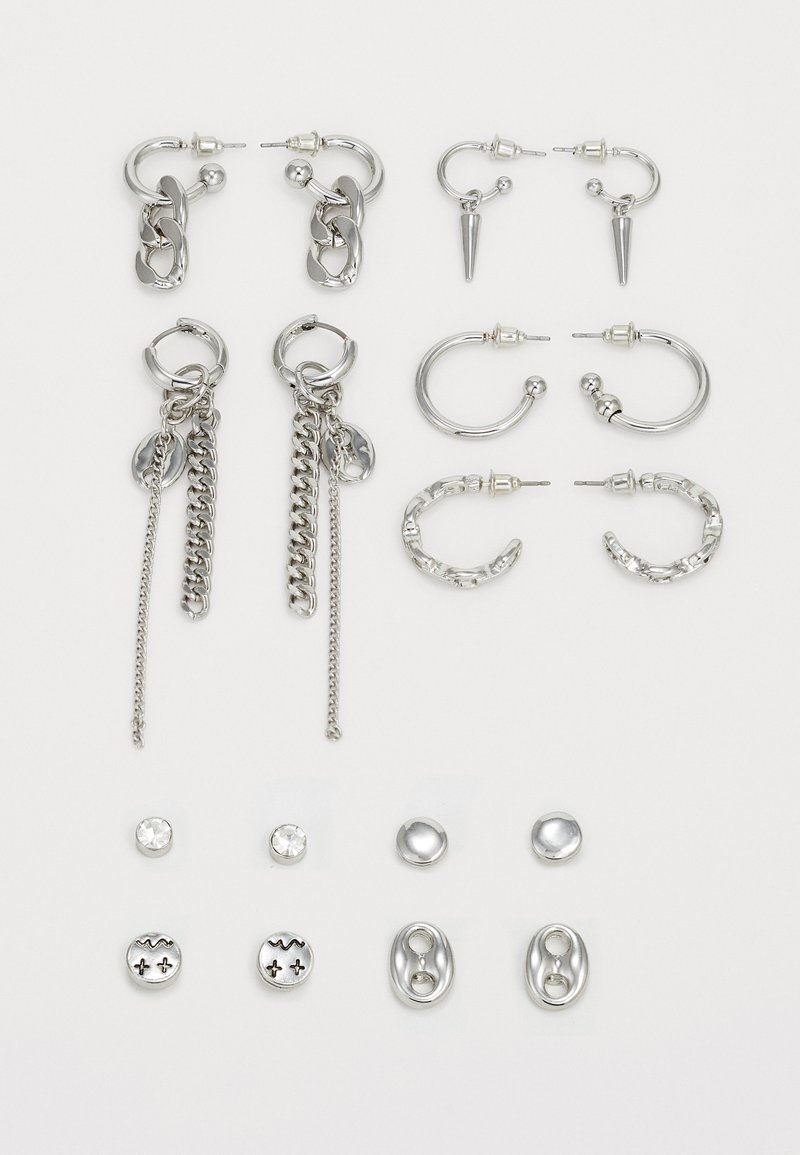 Ensemble de boucles d'oreilles en argent présentant divers designs : créoles, clous, chaînes et pointes avec des finitions texturées et polies.